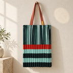 Tote plissettata verde e acqua con fascia arancio e manici ruggine, appesa su una parete avorio.