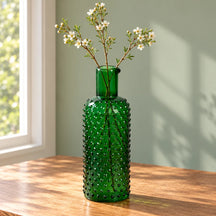 Caraffa verde scuro usata come vaso con tre rami sottili su un tavolo avorio.