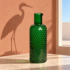 Caraffa verde su una tavola chiara, con l’ombra inattesa di un airone sulla parete.