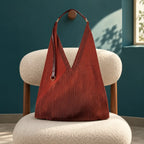Borsa Rubina plissettata color mattone con manico in pelle e anello dorato, su una seduta avorio.