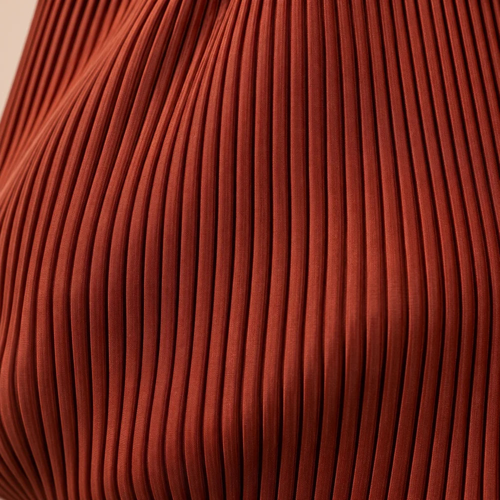 Macro del tessuto color mattone della borsa Rubina, con le pieghe verticali del plissé.