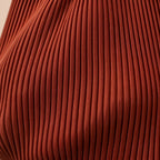 Macro del tessuto color mattone della borsa Rubina, con le pieghe verticali del plissé.