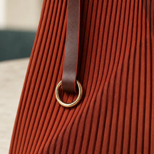Dettaglio della prolunga in pelle marrone e dell’anello dorato della borsa Rubina, sul tessuto plissettato.