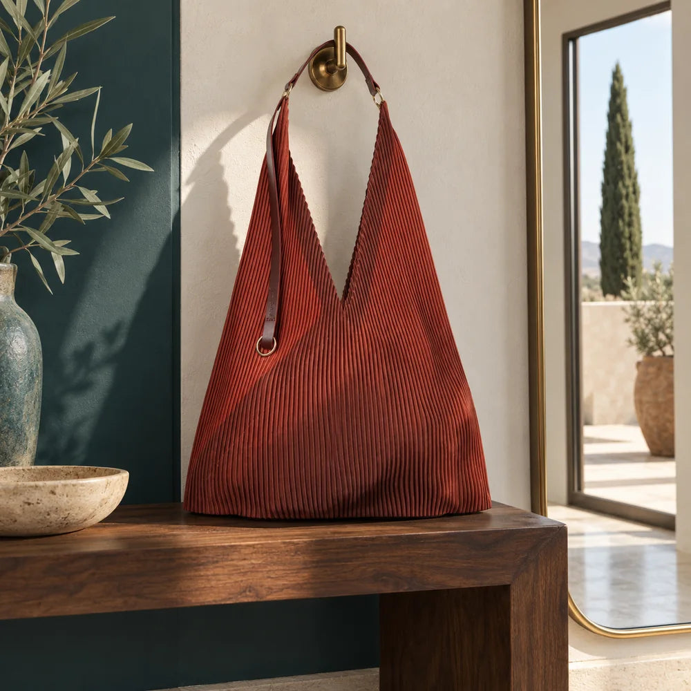 Borsa Rubina su una seduta in noce; uno specchio nell’ingresso riflette un paesaggio con un cipresso isolato.
