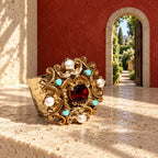 Anello d’Este su un piano avorio, davanti a una piccola porta aperta su un giardino nella parete rossa.