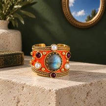 Anello Alhambra Arancio su pietra avorio, davanti a una parete verde e a uno specchio che riflette il cielo.