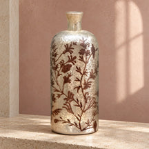 Bottiglia vaso in vetro argentato con decori floreali color ruggine, su pietra avorio.