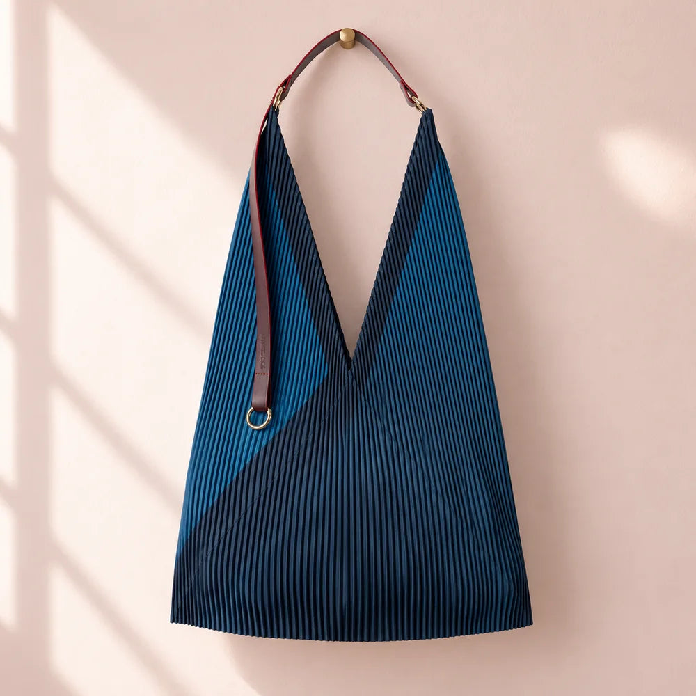 Borsa blu notte con fascia diagonale petrolio e manico in pelle, appesa su parete rosa cipria.