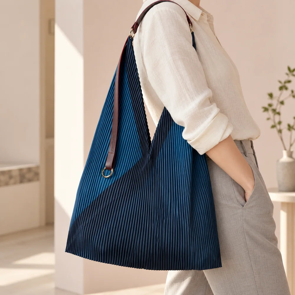 Borsa blu con manico in pelle portata sulla spalla, con la fascia diagonale visibile.