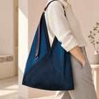 Borsa blu con manico in pelle portata sulla spalla, con la fascia diagonale visibile.