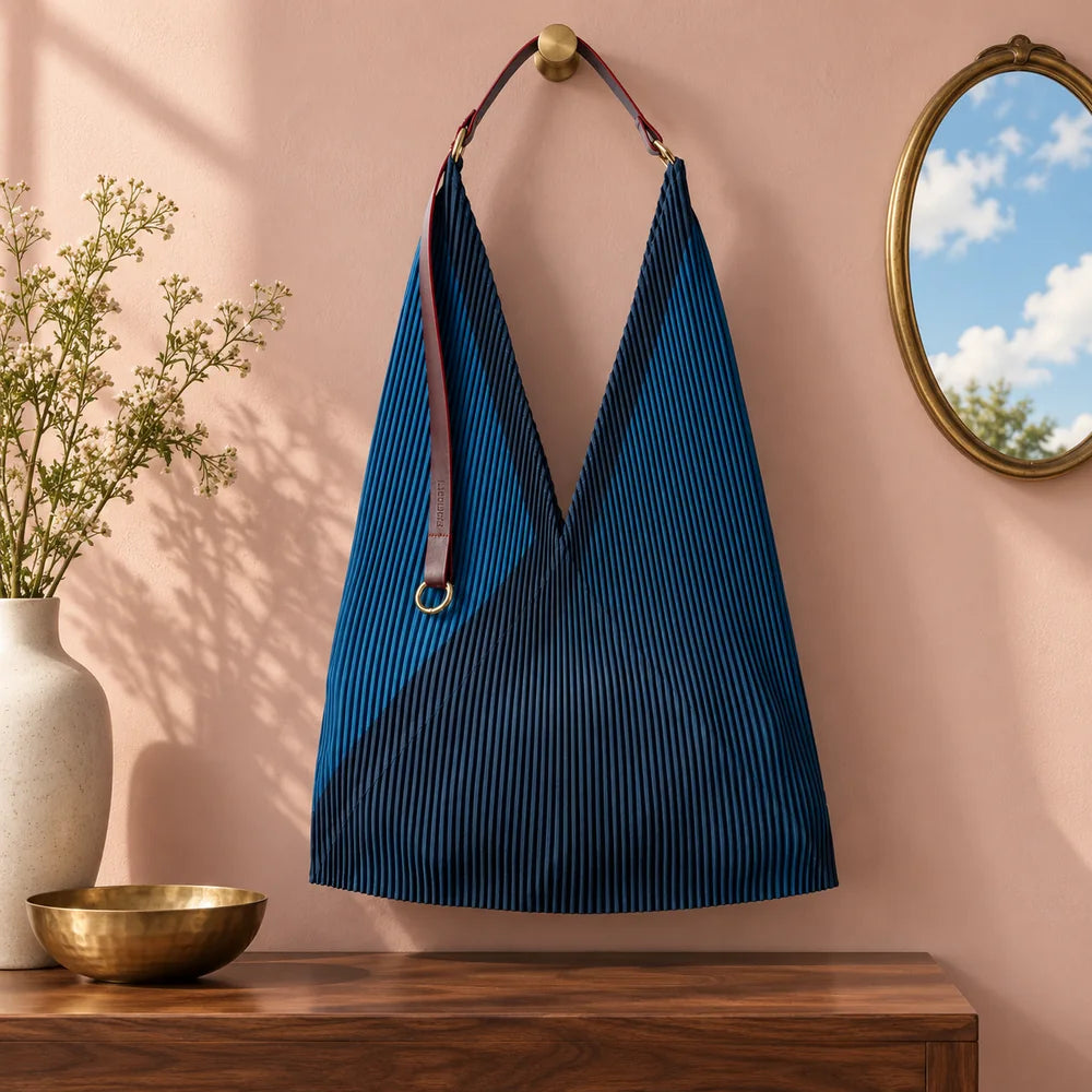 Borsa blu in un interno rosa cipria, accanto a uno specchio che riflette un cielo chiaro.