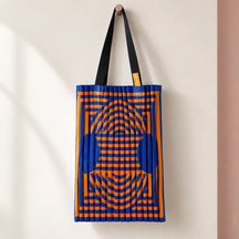 Tote plissettata blu cobalto e arancio, con manici neri, appesa su una parete avorio.