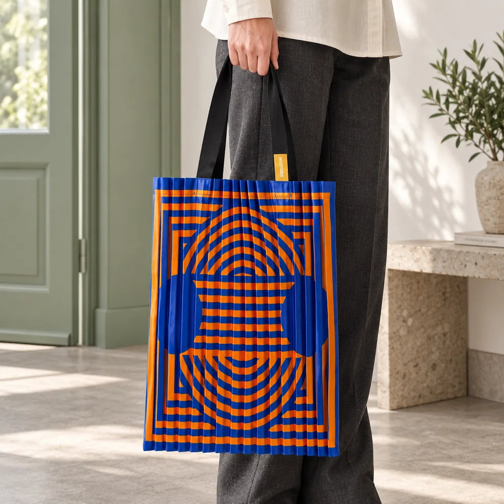 Tote blu e arancio portata in mano, con il disegno geometrico e i manici neri visibili.