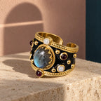 Alhambra Nero con labradorite, perle e piccoli decori rossi su pietra avorio; ombra di arco interrotta sul fondo.