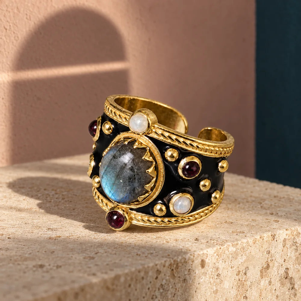 Alhambra Nero con labradorite, perle e piccoli decori rossi su pietra avorio; ombra di arco interrotta sul fondo.