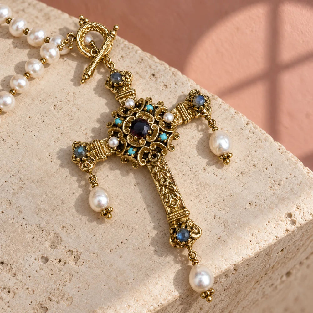 Croce Castel in ottone dorato con pietre blu, cristallo scuro e tre perle pendenti, su pietra avorio.