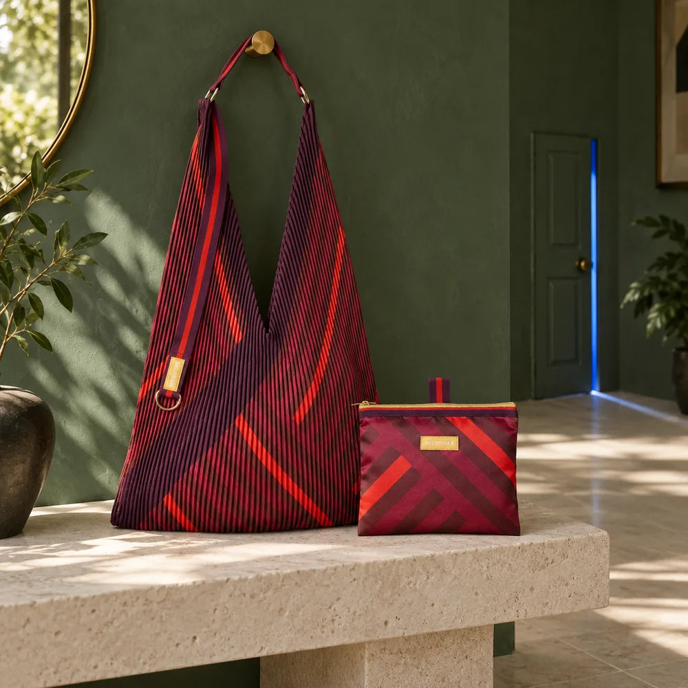 Borsa Granata plissettata e pochette coordinata su una panca avorio, in un ingresso verde con una piccola porta luminosa.