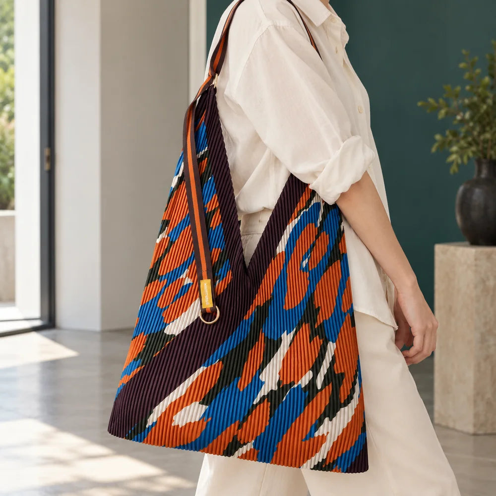 Borsa camouflage blu e arancio portata sulla spalla, con il manico in tessuto e l’anello dorato.