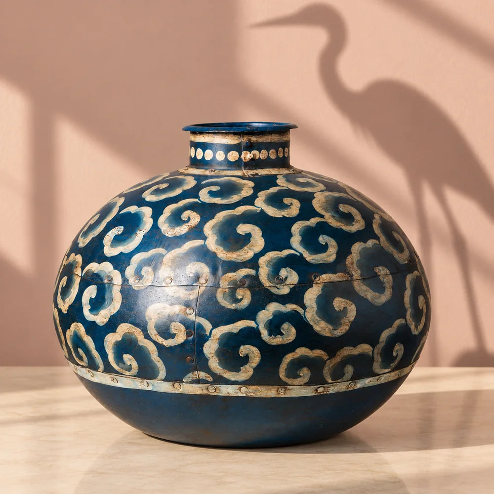 Vaso decorativo blu in ferro con motivi beige, su un piano avorio davanti a una parete rosa.