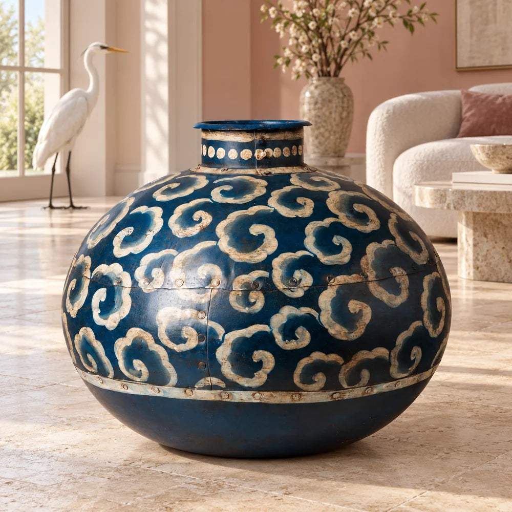 Vaso blu in ferro con motivi beige, in una stanza luminosa con un airone bianco sullo sfondo.