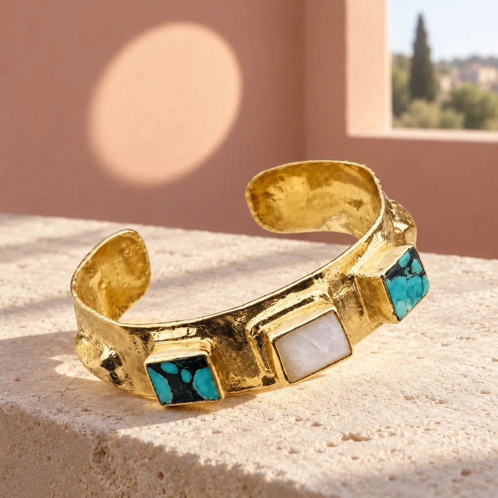 Bracciale Templier aperto in ottone dorato martellato, con turchesi venati e pietra di luna, su una mensola avorio.
