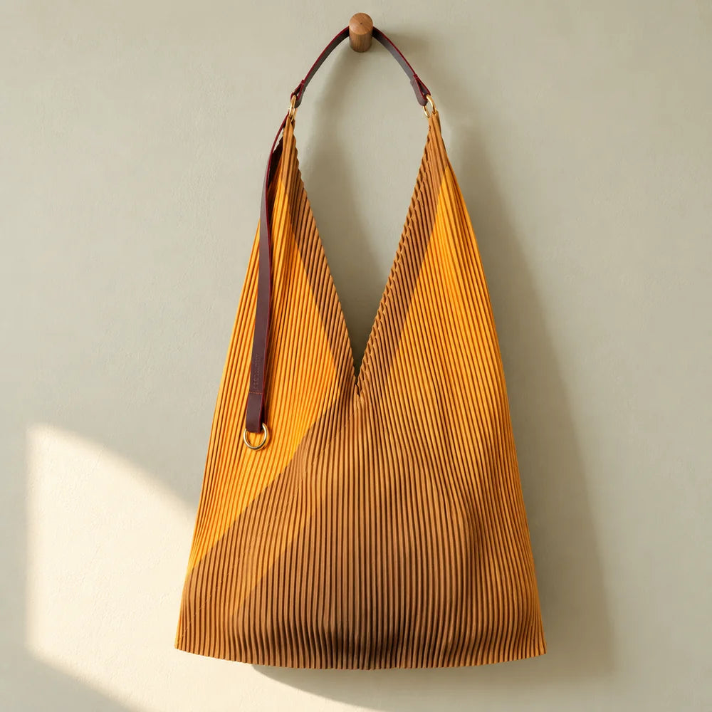 Borsa ocra e giallo arancio con manico in pelle, appesa su una parete salvia.