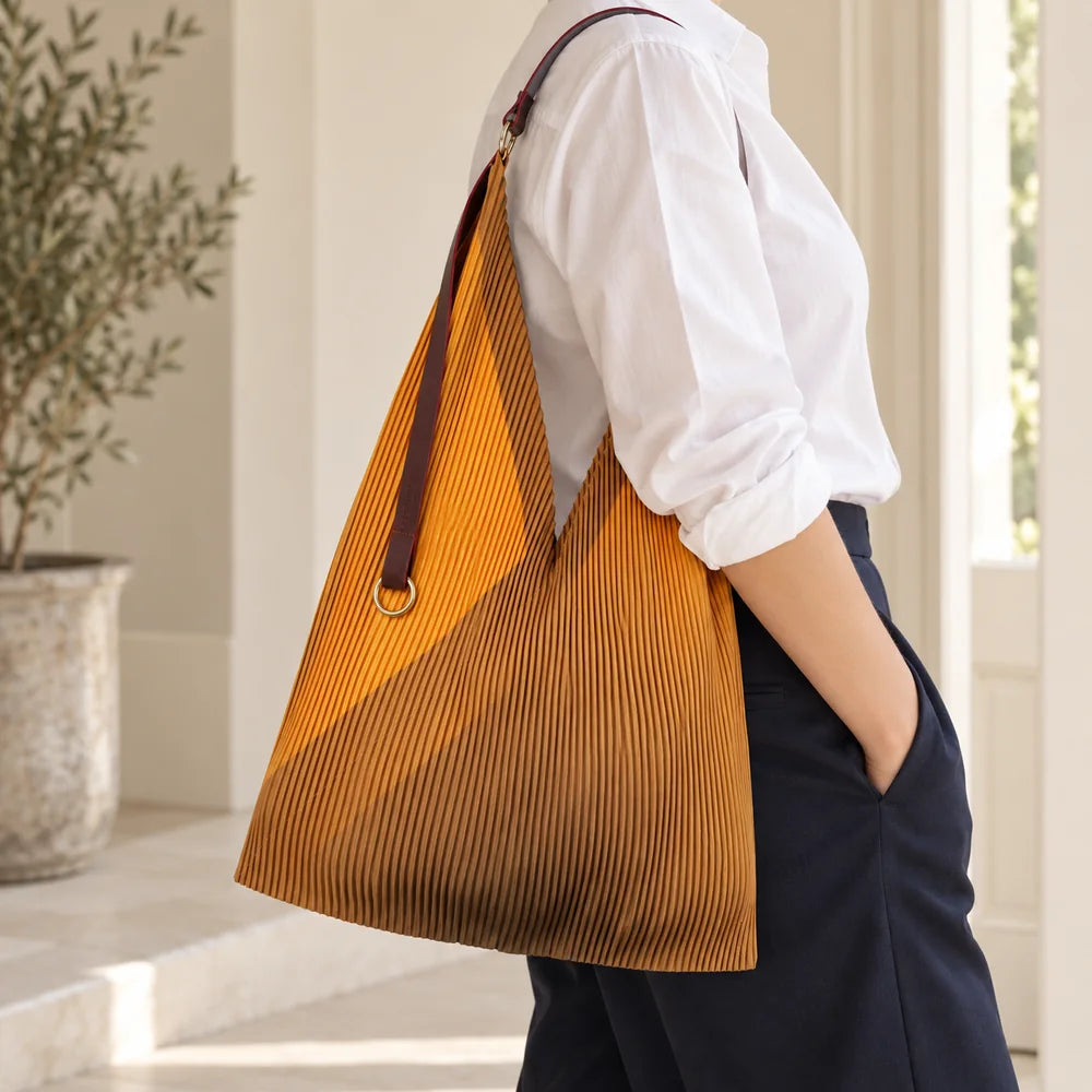 Borsa gialla e ocra portata sulla spalla, con manico in pelle e anello dorato.