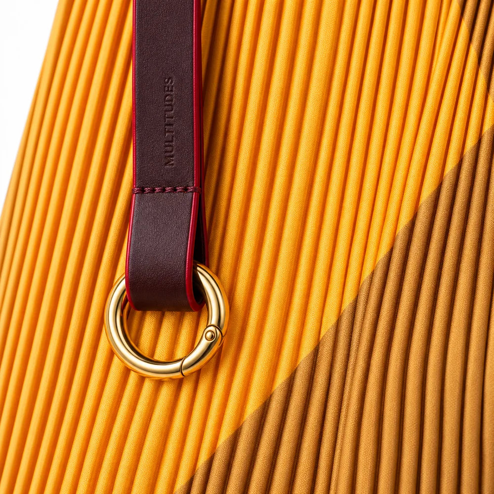 Dettaglio del manico in pelle marrone con l’anello moschettone dorato della borsa gialla.