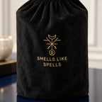 Sacca nera inclusa con simbolo dorato e scritta Smells Like Spells, dettaglio della candela Medio Oriente.