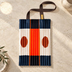 Tote blu scuro, crema e arancio con due cerchi ruggine, distesa su pietra avorio.