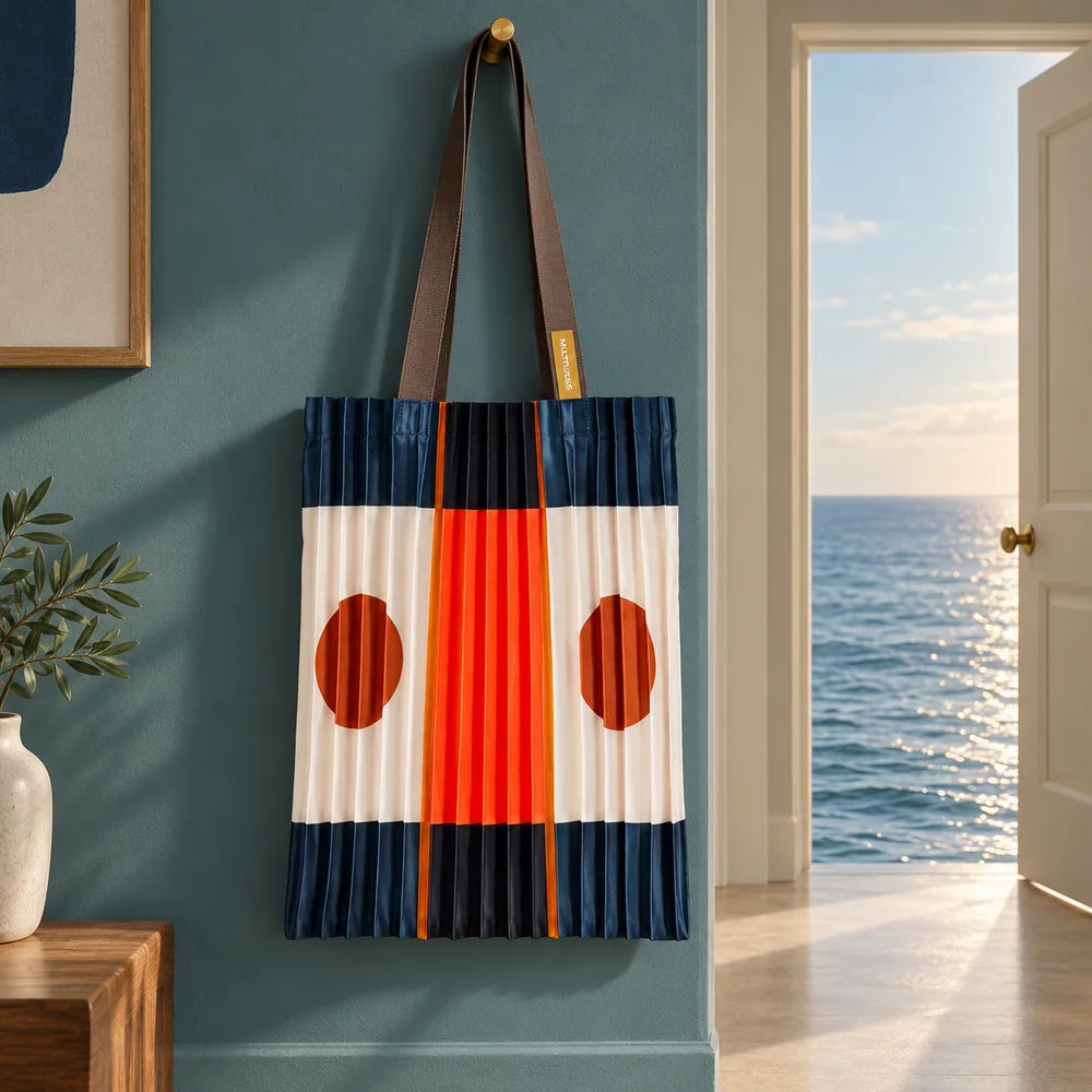 Tote blu scuro e arancio appesa in un interno petrolio, accanto a una porta aperta sul mare.