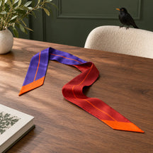 Twilly viola e bordeaux appoggiato a una scrivania in noce in un atelier verde, con un piccolo uccello sulla sedia.