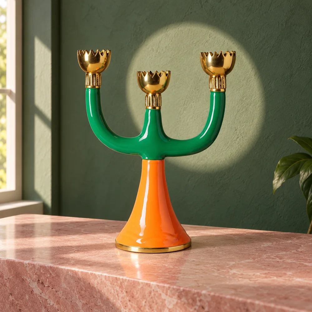 Candelabro Retro per tre candele, con bracci verdi, coppe dorate e piede arancione, su una console rosa.