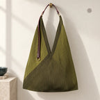 Borsa verde oliva plissettata con manico in pelle e anello dorato, appesa su parete avorio.