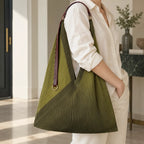 Borsa verde con manico in pelle portata sulla spalla, con l’anello dorato visibile.
