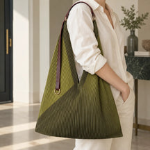 Borsa verde con manico in pelle portata sulla spalla, con l’anello dorato visibile.